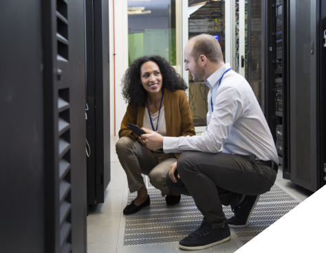 A woman and man crouching in front of a server rack